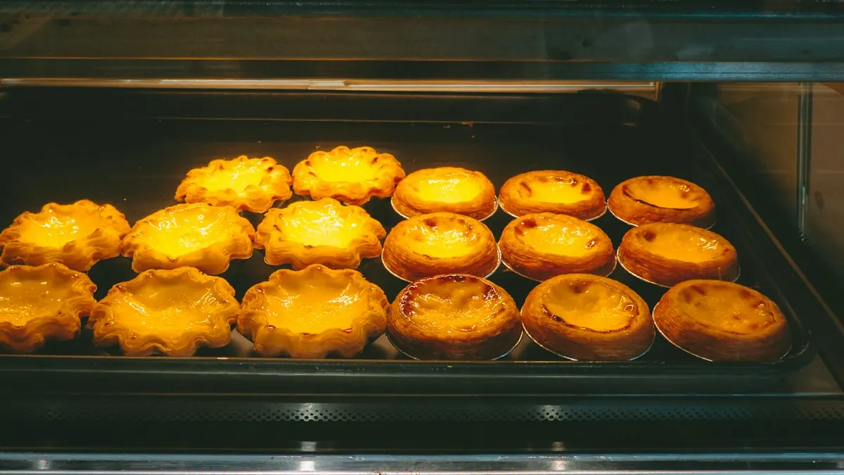 Rows of freshly baked egg tarts glowing under a warm display light