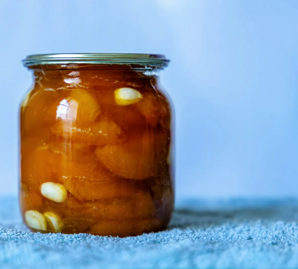 A glass jar of golden preserved fruit standing on a blue cloth